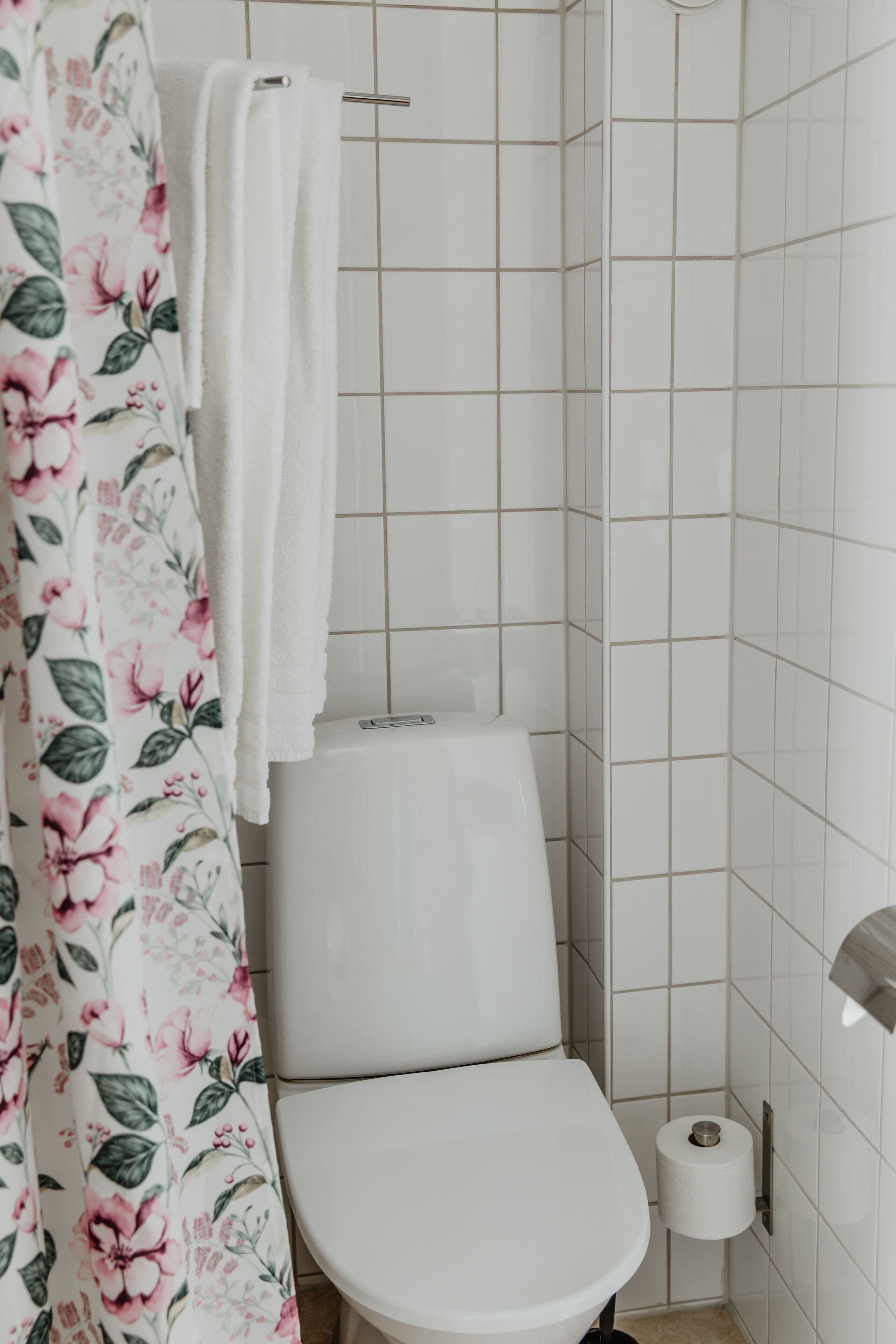 A bathroom with a toilet, a shower curtain with floral patterns, and a white towel hanging on a rack.