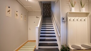 Una escalera con barandilla blanca, una puerta con el número 21 y un perchero de pared con ganchos.