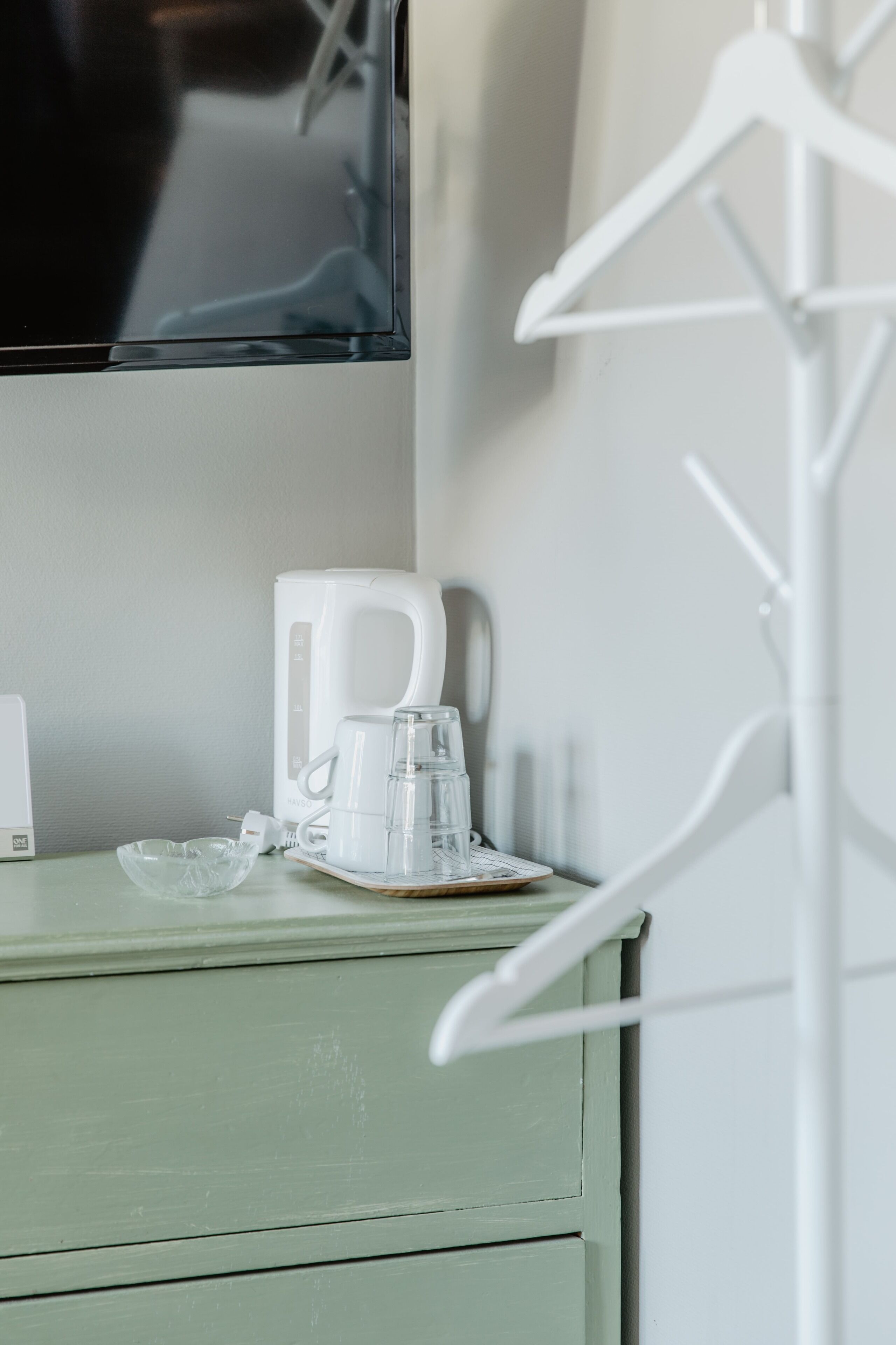 Una kitchenette con una cafetera, una jarra de vidrio y un tazón sobre un mueble verde.
