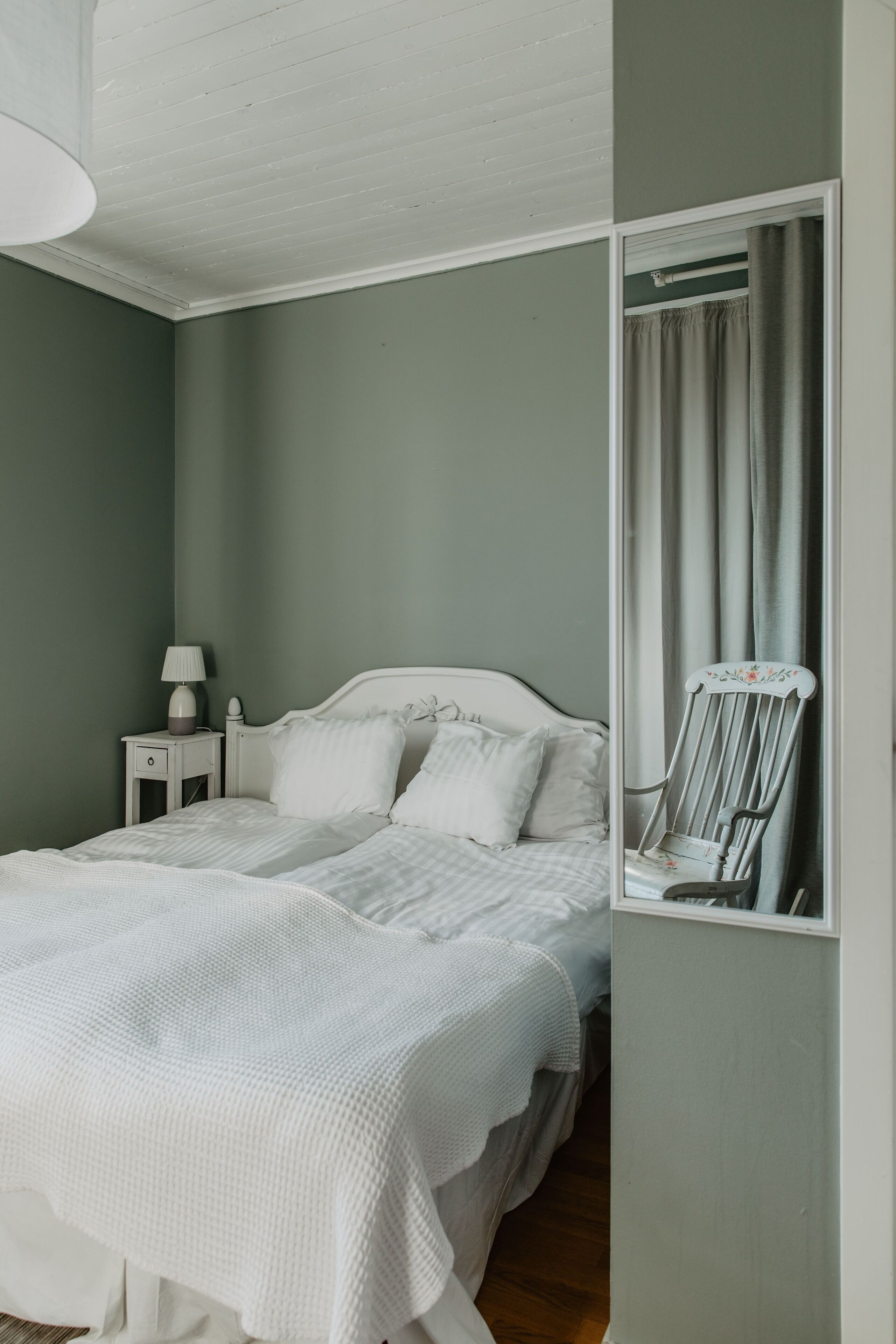 A bedroom with a bed, nightstand, lamp, and a mirror.