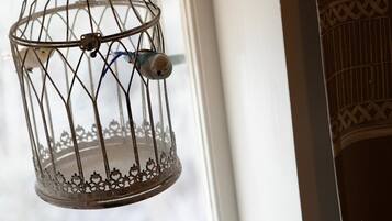 A metal birdcage hanging by a ring, with a bird inside, near a window with a white frame.