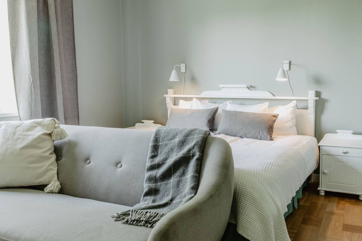 A bedroom with a bed, a nightstand, a lamp, and a sofa.