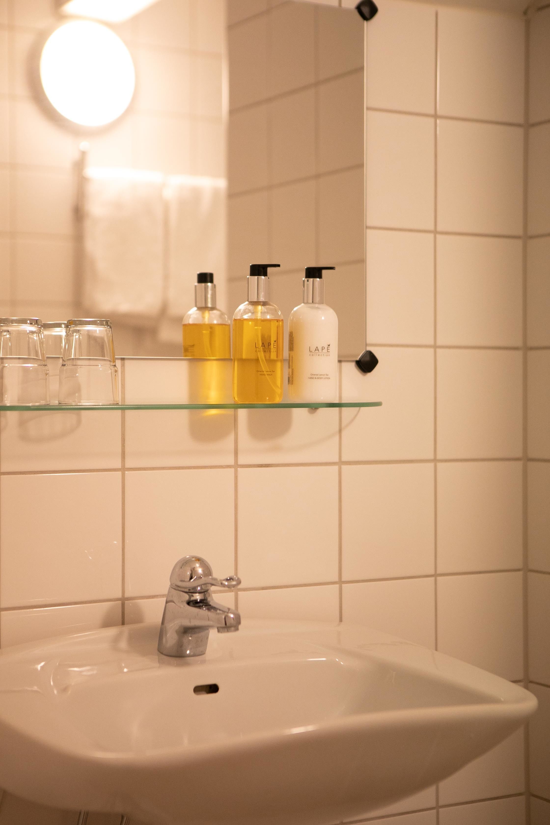 Un baño con lavamanos blanco, un espejo y un estante con artículos de aseo.