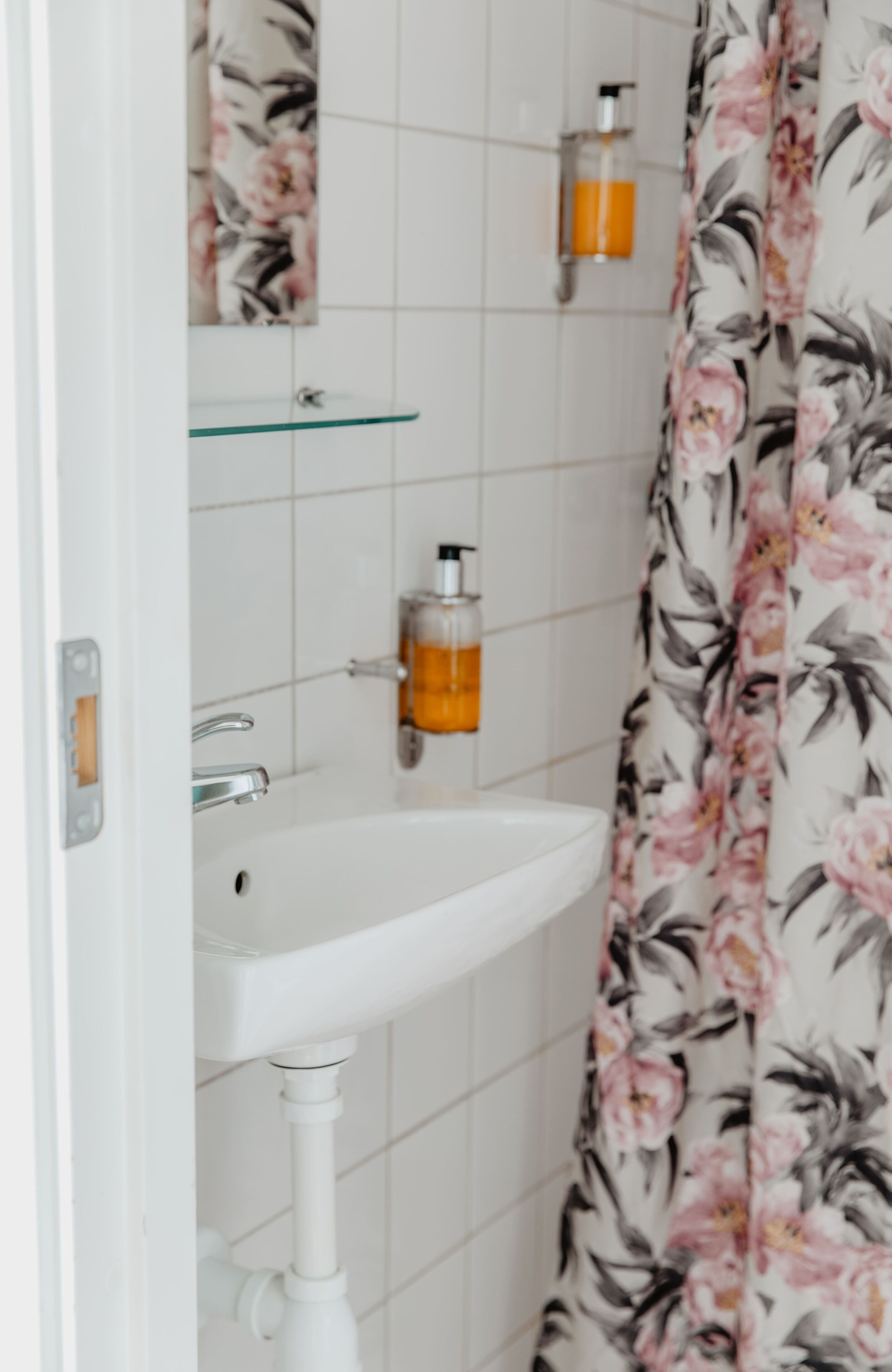 A bathroom with a white sink, a glass shelf, and a floral shower curtain.