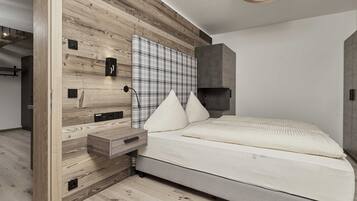 A modern bedroom with a wooden headboard, a large plaid-patterned wall hanging, a bed with white bedding, and a bedside table with a drawer.