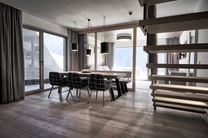 A modern dining area with a wooden table, plaid chairs, and large windows offering a mountain view.