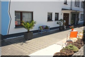 A building with a white exterior, a paved walkway, a bench, and potted plants. - Ferienwohnungen Cella (Zell (Mosel))