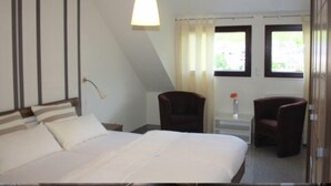 A hotel room with a bed, two chairs, a desk, a lamp, and a window with curtains. - Ferienwohnungen Cella (Zell (Mosel))