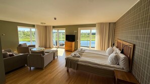 Ein Hotelzimmer mit einem großen Bett, einer Sitzecke, einem Fernseher und einem Balkon mit Seeblick.