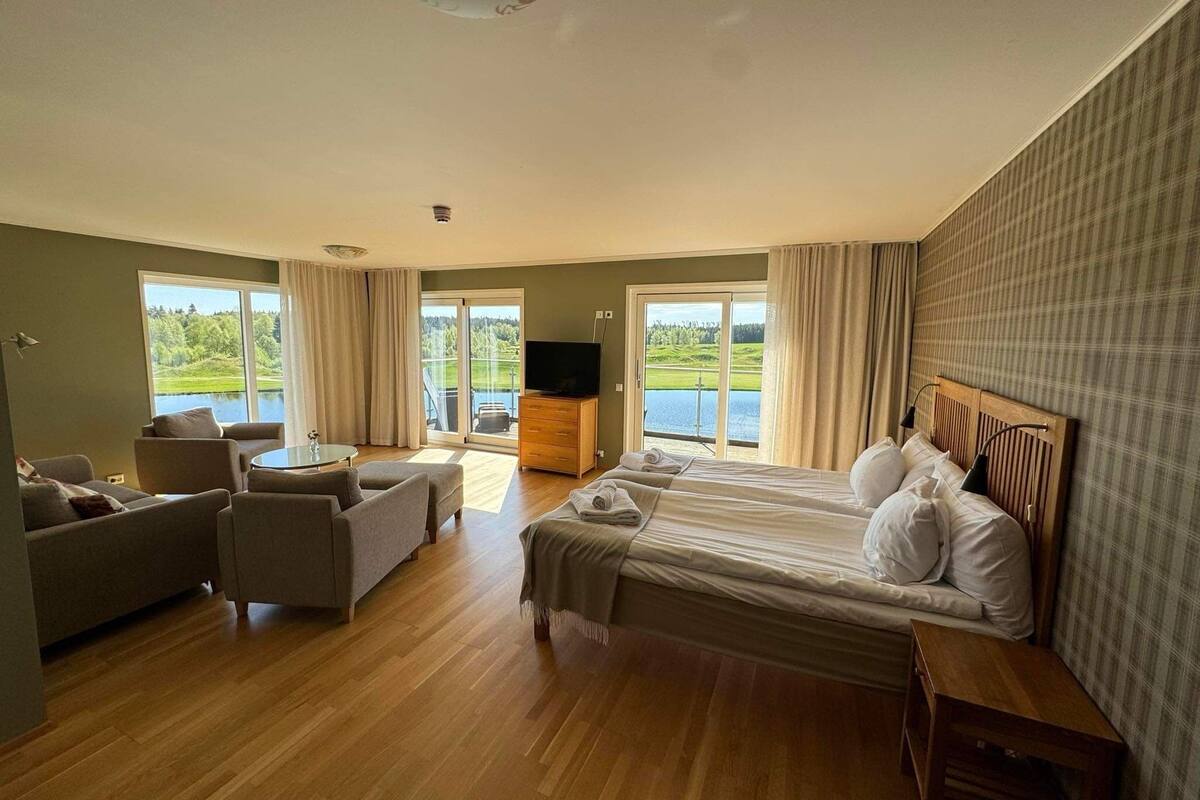 A hotel room with a large bed, a sofa, a TV, and a balcony with a view of a lake.