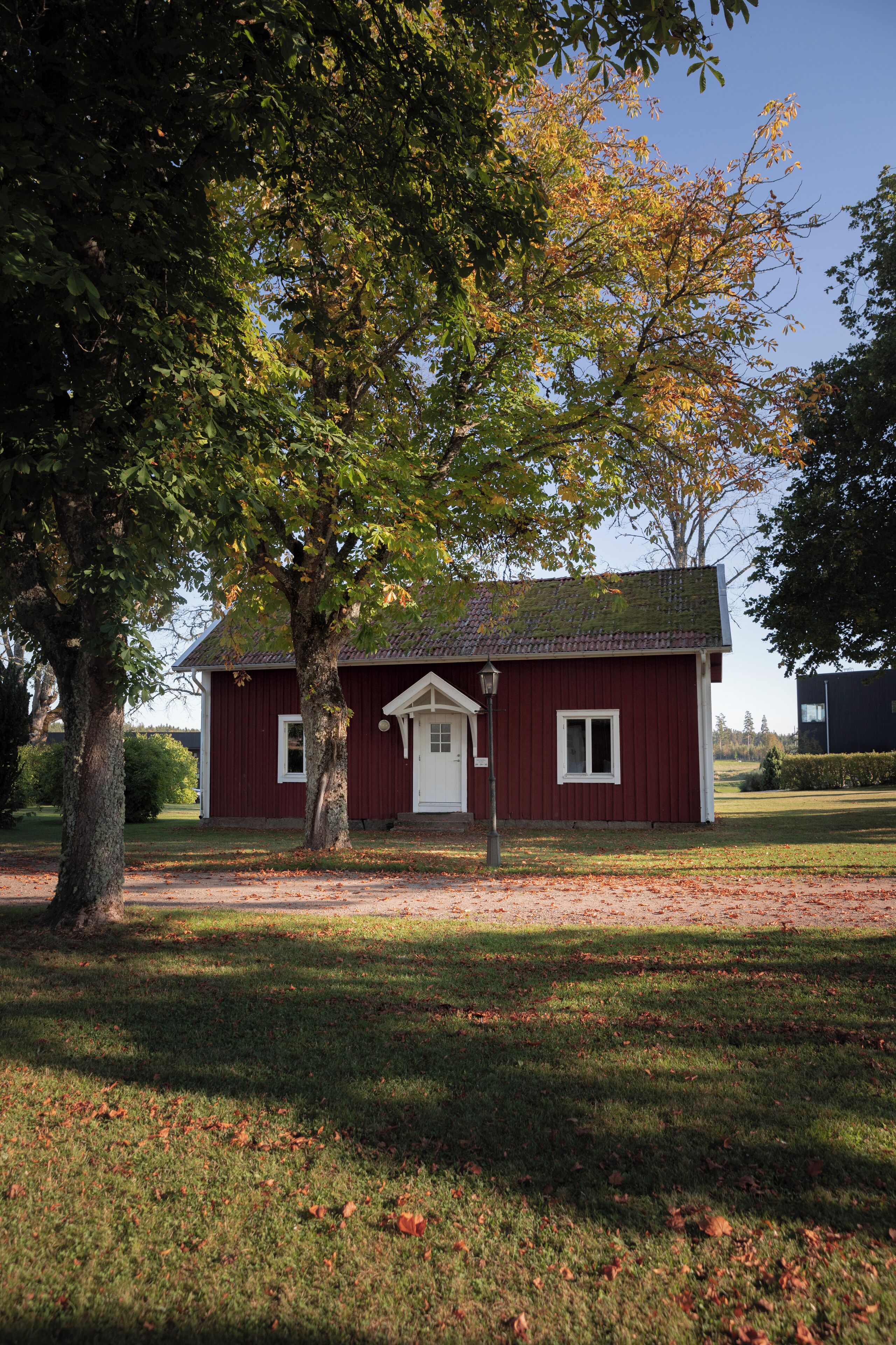 A red building with a white door and windows, surrounded by grass and trees.