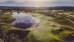 Ein Golfplatz mit einem großen Teich, einer Brücke und bewaldeter Landschaft im Hintergrund.