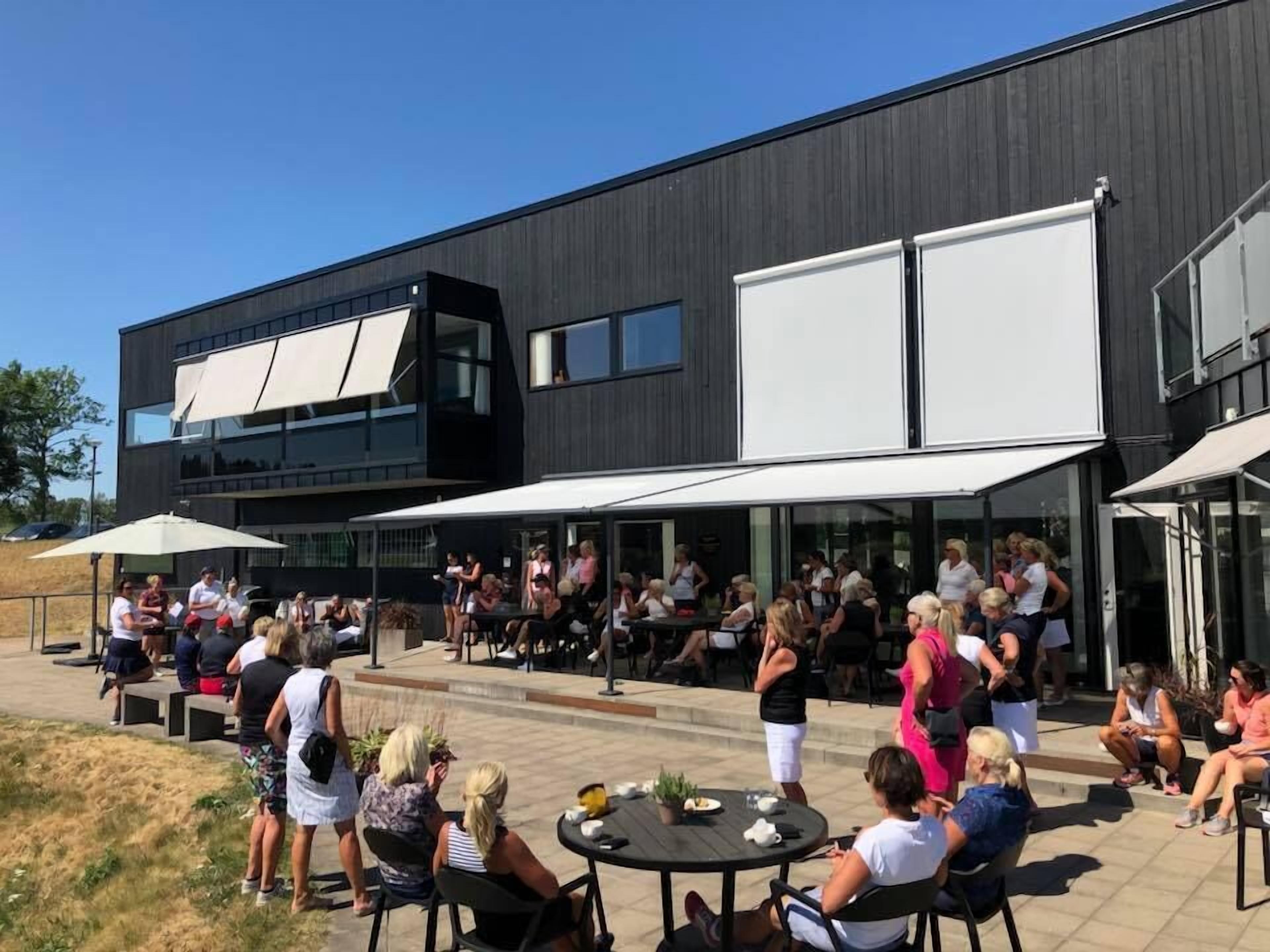 Un espace extérieur aménagé avec des tables et des chaises, un bâtiment moderne doté de grandes fenêtres et un ciel dégagé.