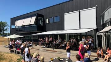 Un espace extérieur aménagé avec des tables et des chaises, un bâtiment moderne doté de grandes fenêtres et un ciel dégagé.