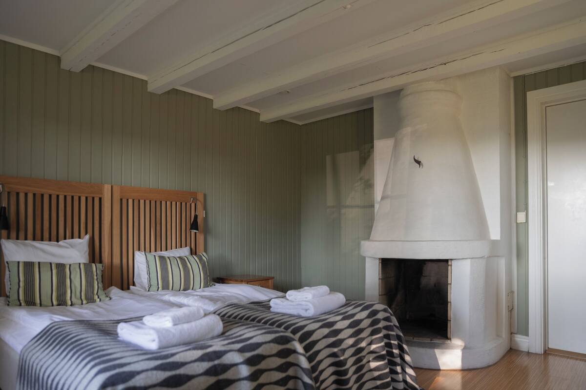 A hotel room with a bed, a wooden headboard, a fireplace, and a green-striped wall.