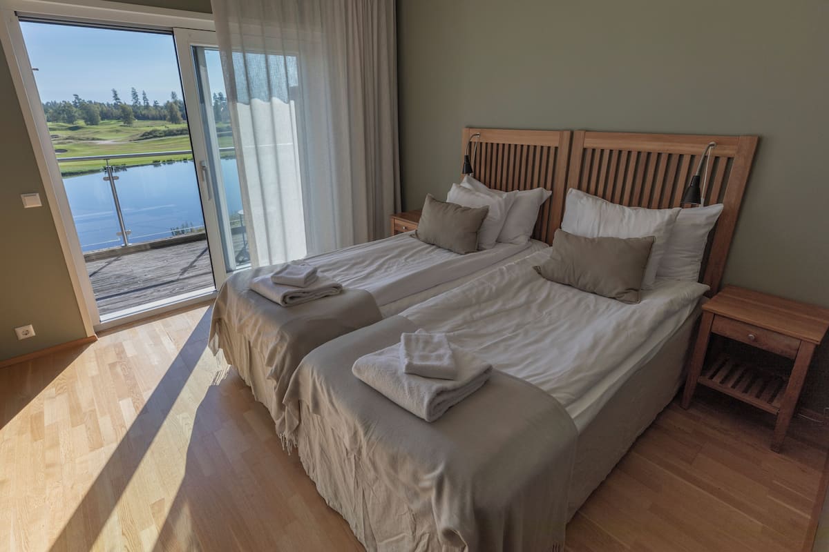 A double bed with a wooden headboard, two bedside tables, and a view of a lake through a sliding glass door.