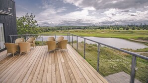 Eine Holterrasse mit Korbstühlen und Blick auf einen Golfplatz und einen See.