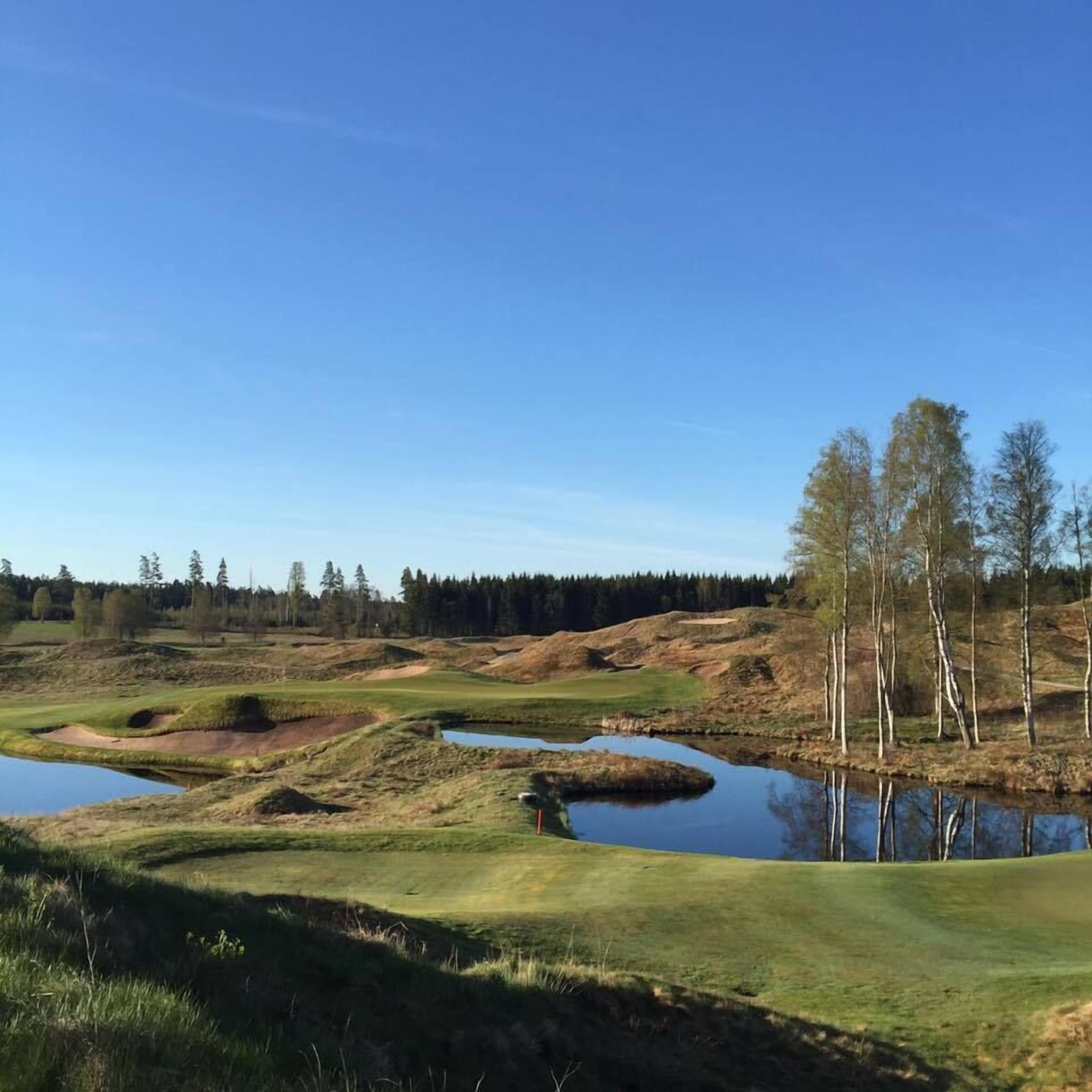 A golf course with bunkers, water hazards, and a clear blue sky.