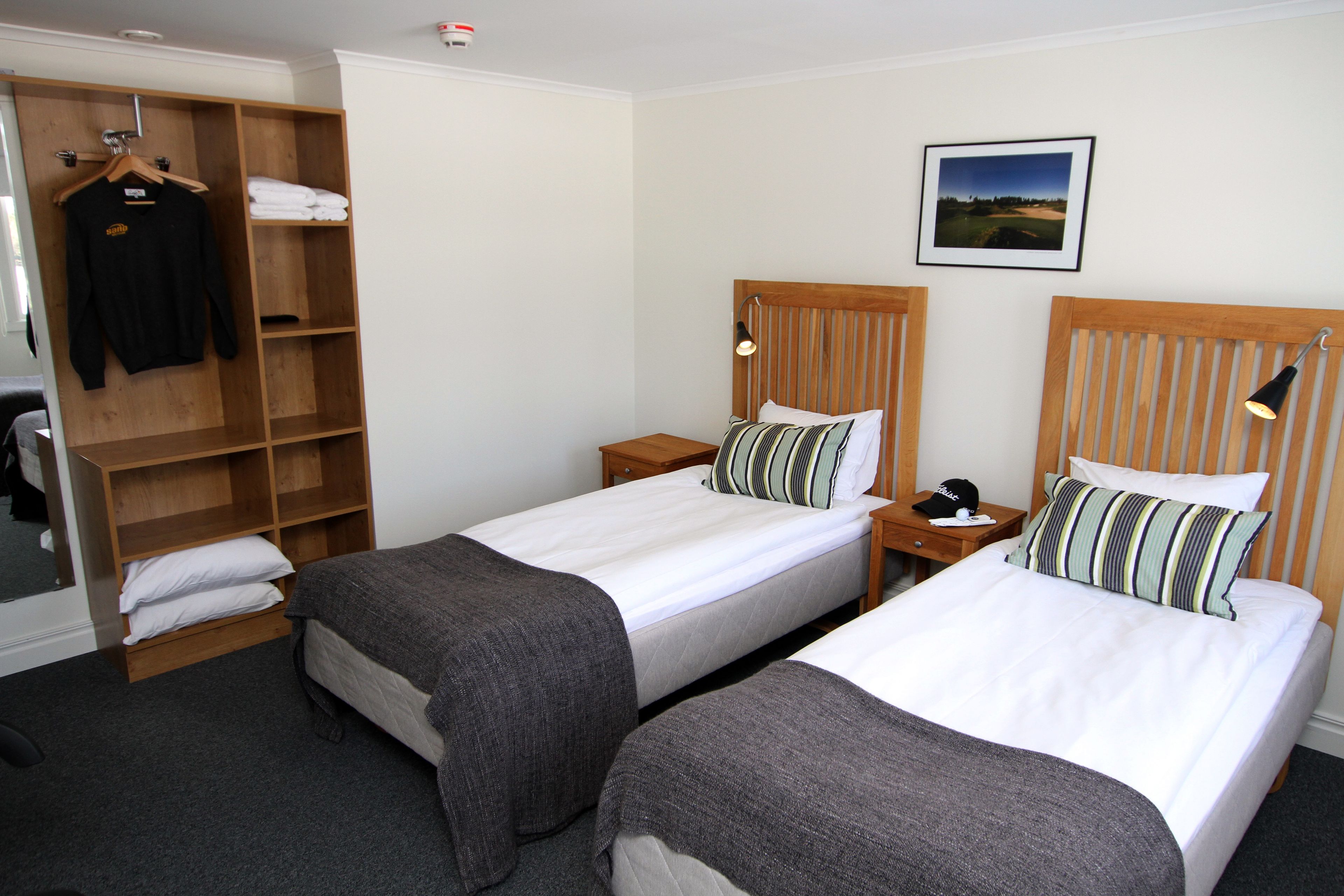 A hotel room with two single beds, a wooden wardrobe, a small table with a lamp, and a framed picture on the wall.