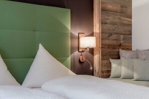 A hotel room with a green upholstered headboard, a wall-mounted lamp, and a bed with white bedding. - Vacation apartment Melisande 1 - The Peak Sölden (Sölden)