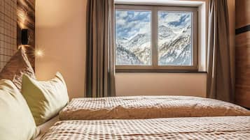 A bedroom with a bed, pillows, a window with a mountain view, and a wall-mounted light.