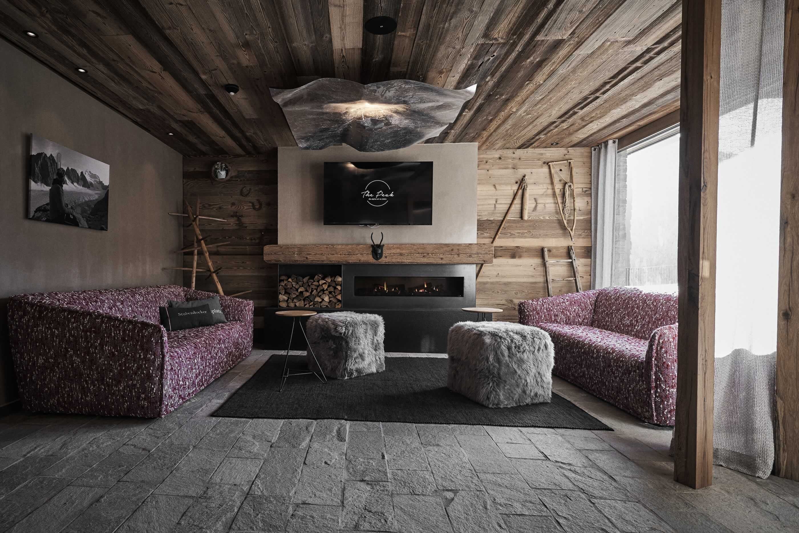 A cozy living room with a fireplace, wooden ceiling, and a TV mounted above it.