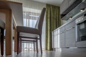A modern kitchen with a built-in oven, a dining area with a chair, and a window with sheer curtains. - Vacation apartment Melisande 1 - The Peak Sölden (Sölden)