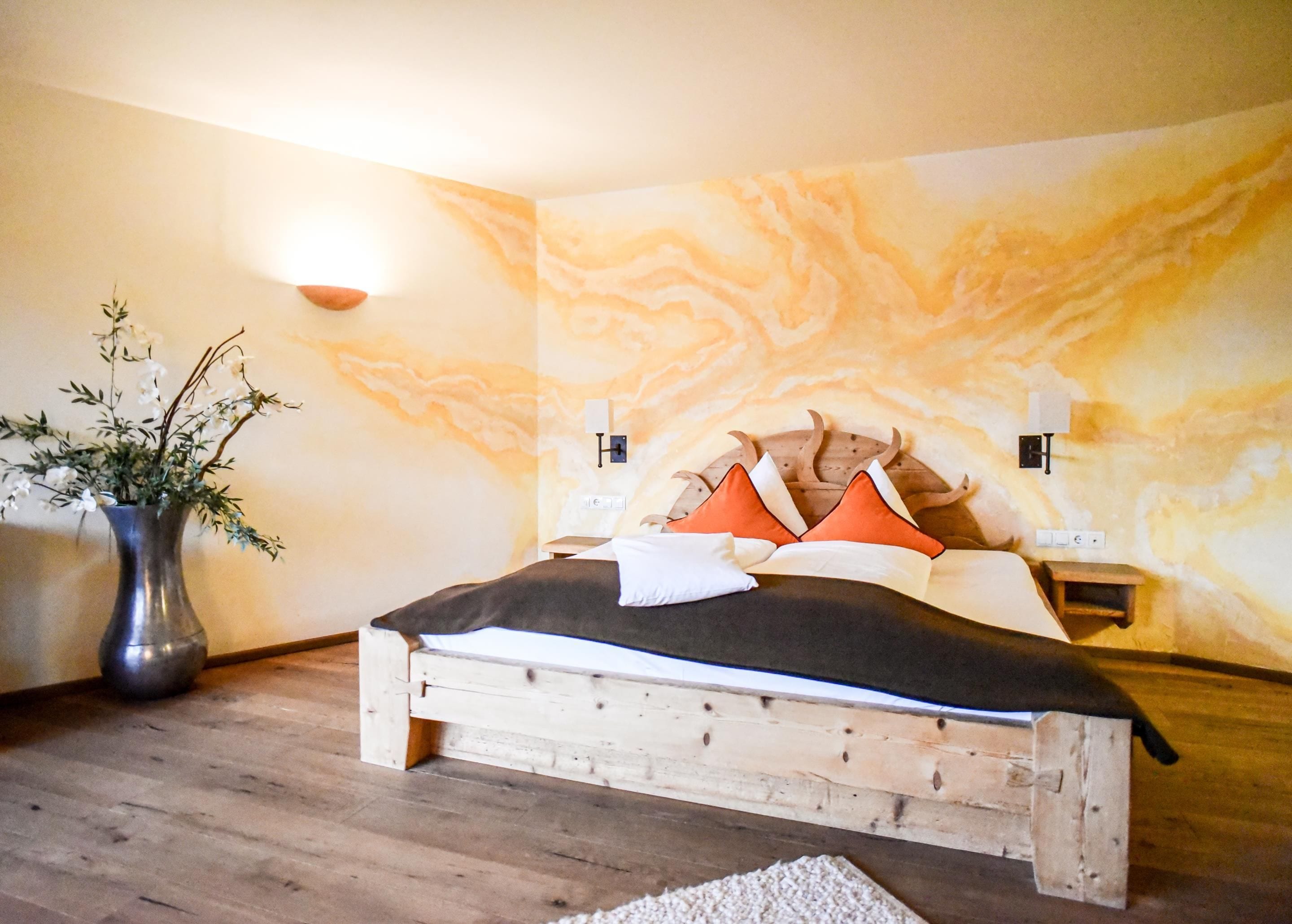 Ein hölzernes Bett mit Kopfteil, eine Vase mit Blumen und eine Wand mit Marmor-Optik.