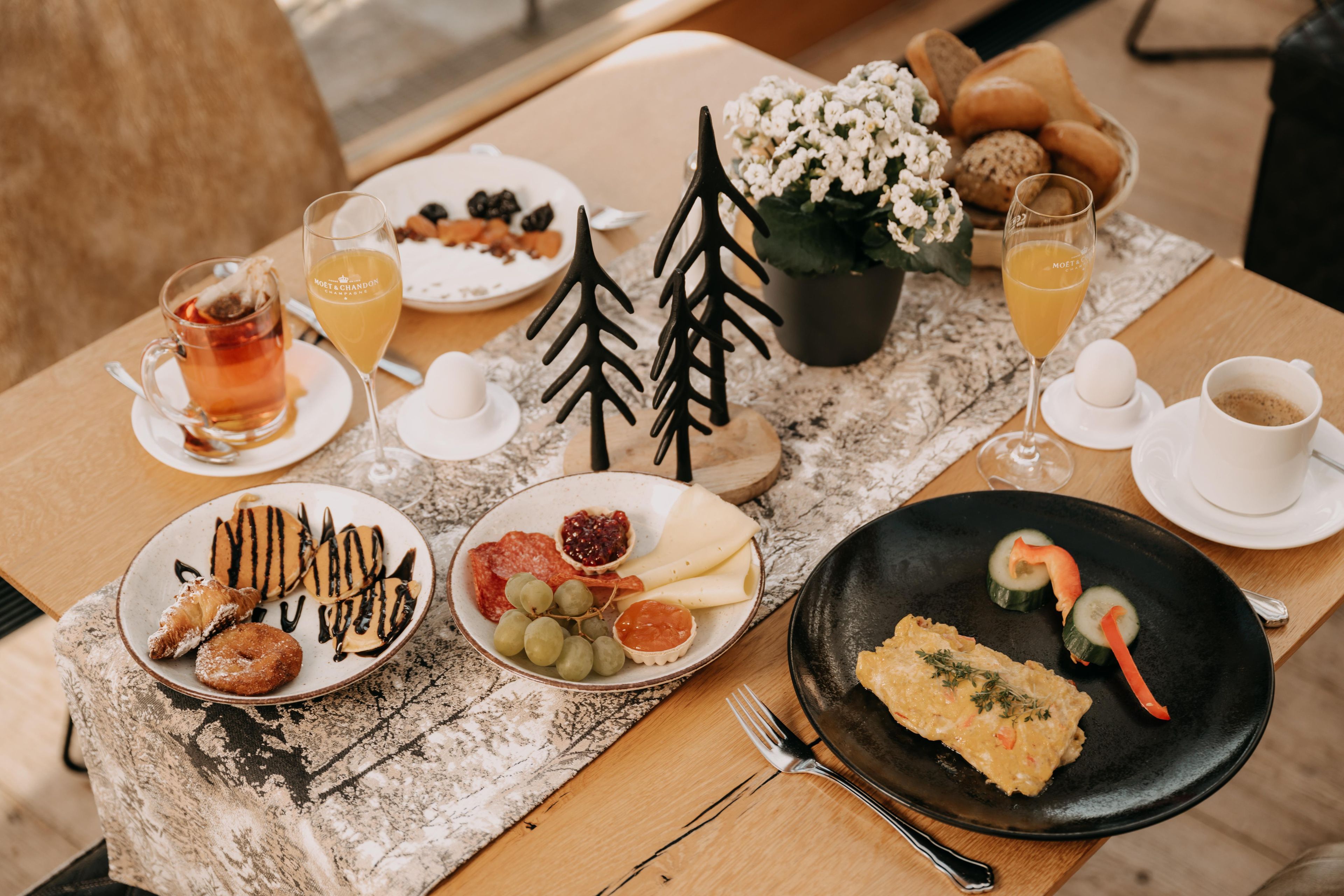 A breakfast table with various food items, drinks, and a small decorative tree.
