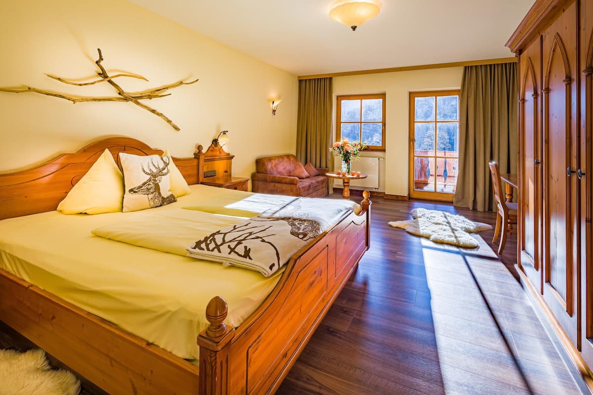 Un dormitorio amplio con una cama grande, un cabecero de madera, una mesita de noche, una silla, una ventana con cortinas y vistas al exterior.
