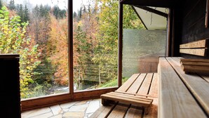 Un banco de madera y suelo de piedra dentro de una habitación con ventanales amplios que dan a un bosque.