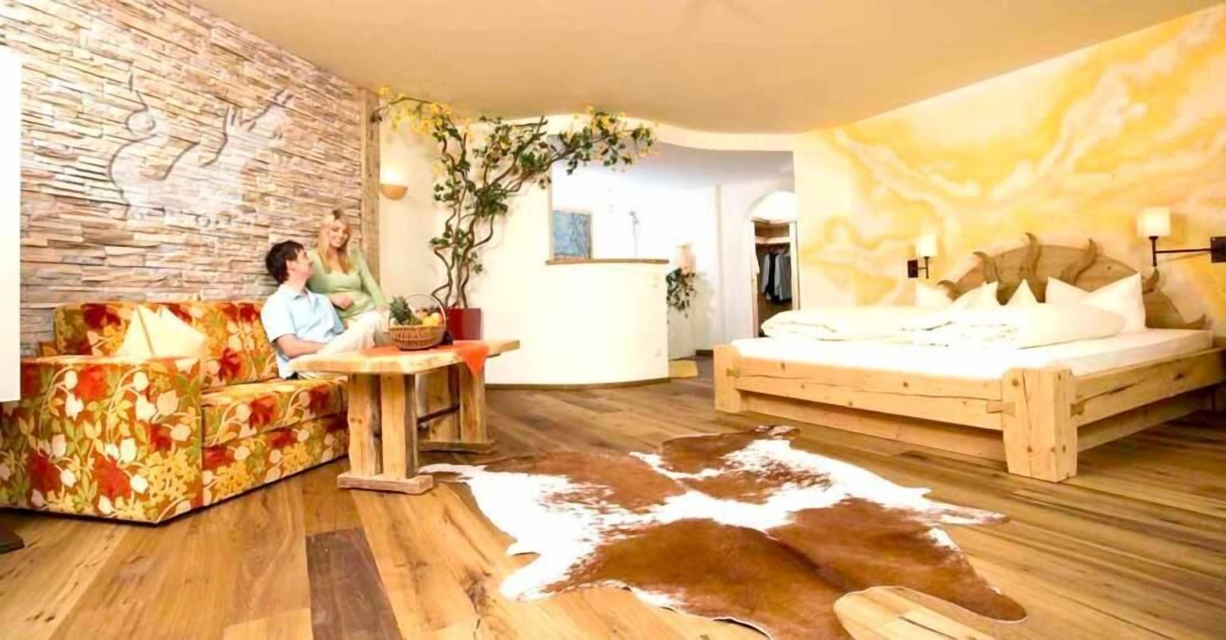 A cozy room with a wooden floor, a sofa with floral upholstery, a wooden bed, and a cowhide rug.