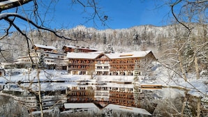 Un amplio y espacioso lodge de madera de varios pisos con balcones, ubicado junto a un lago tranquilo y paisajes nevados.