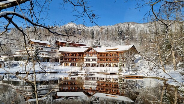Un amplio y espacioso lodge de madera de varios pisos con balcones, ubicado junto a un lago tranquilo y paisajes nevados.
