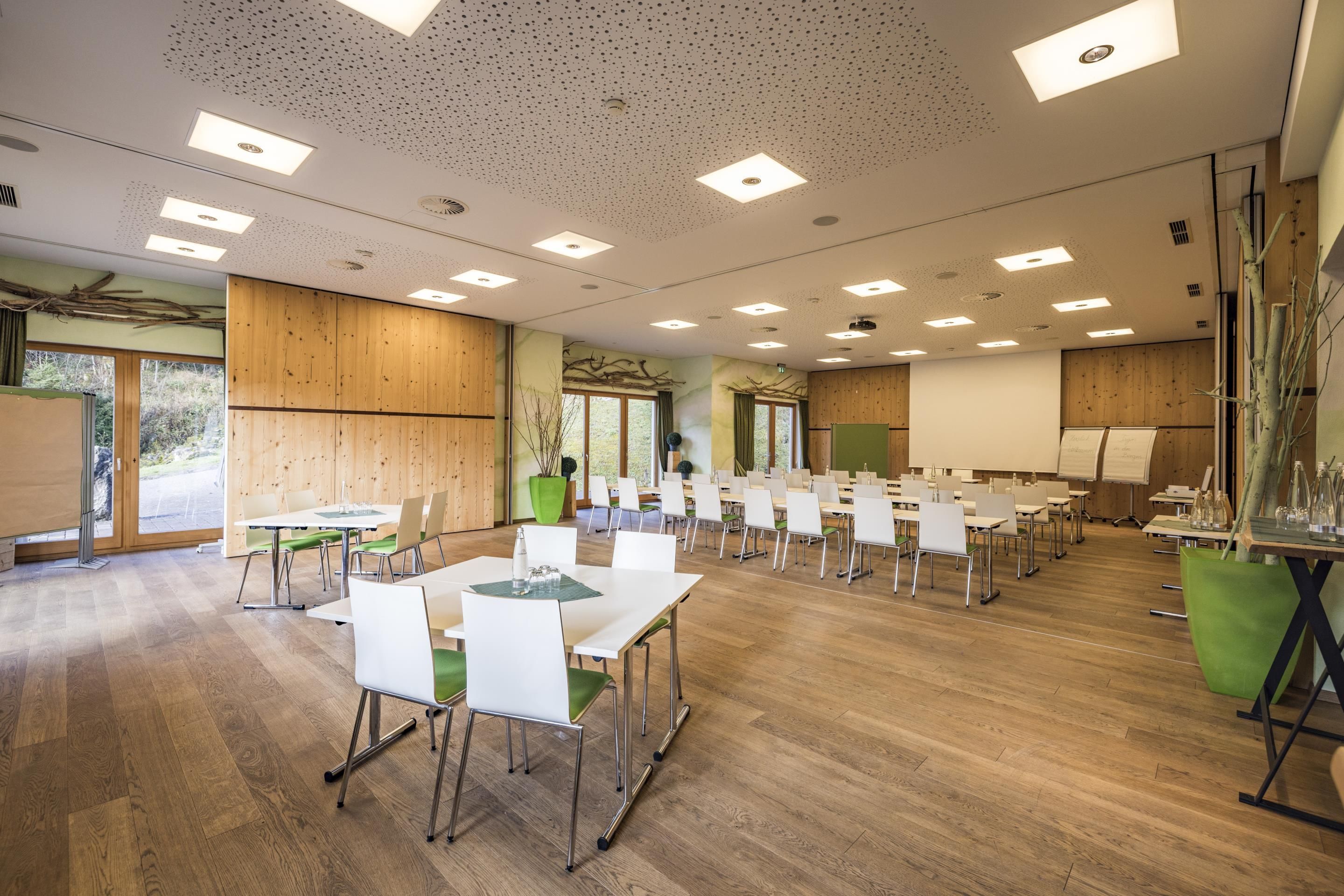 Ein geräumiger Konferenzraum mit mehreren Tischen und Stühlen, Holzwänden und großen Fenstern.