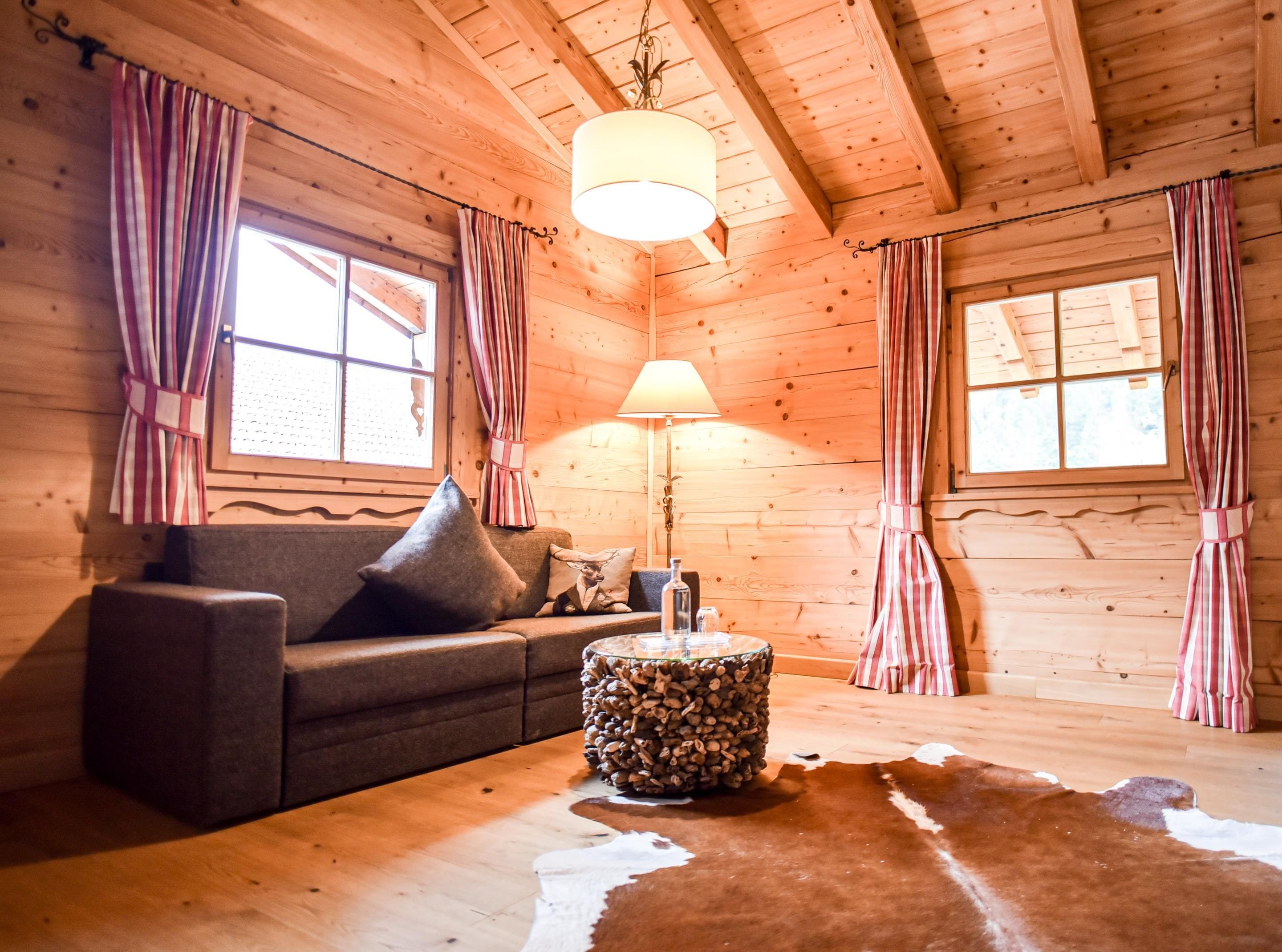 A cozy cabin interior with a wooden ceiling, a sofa with cushions, a round coffee table, and a cowhide rug.