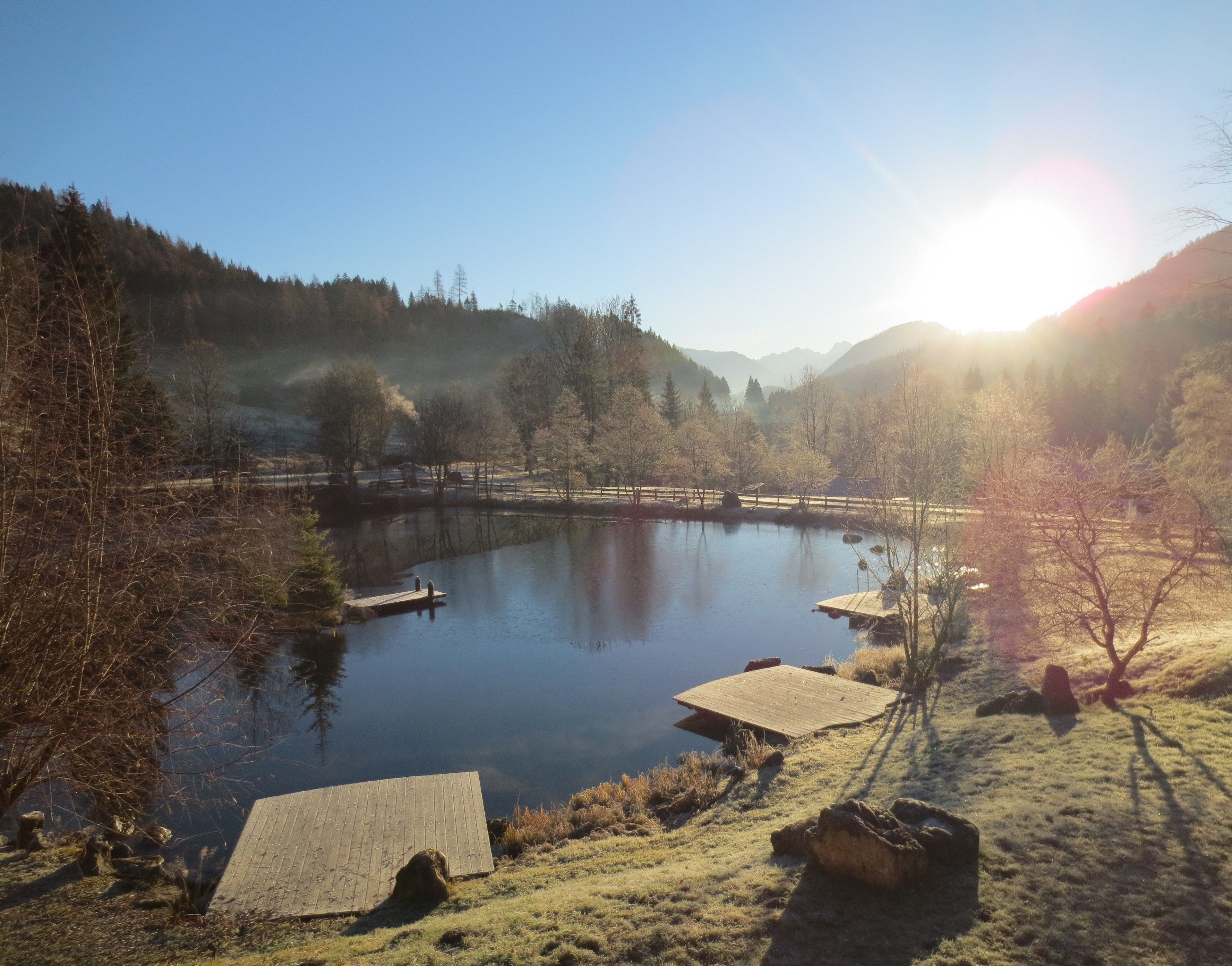 A serene lakeside scene with a wooden dock extending into the water, surrounded by trees and hills.