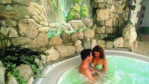 Un jacuzzi con un muro de piedra al fondo, rodeado de follaje.