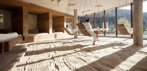 A room with wooden walls and large windows, a bed, and two people relaxing on swings. - Feuriger Tatzlwurm Berghotel & Spa, BW Signature Collection (Oberaudorf)