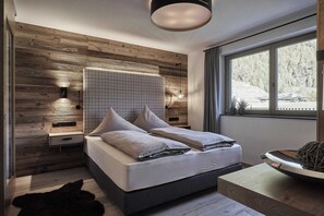 A modern bedroom with a wooden wall, a large window, a bed with pillows, a bedside table, and a wall-mounted light fixture.