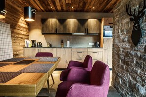 A modern kitchen with wooden cabinets, a dining table with purple chairs, and a stone wall with a deer head decoration.