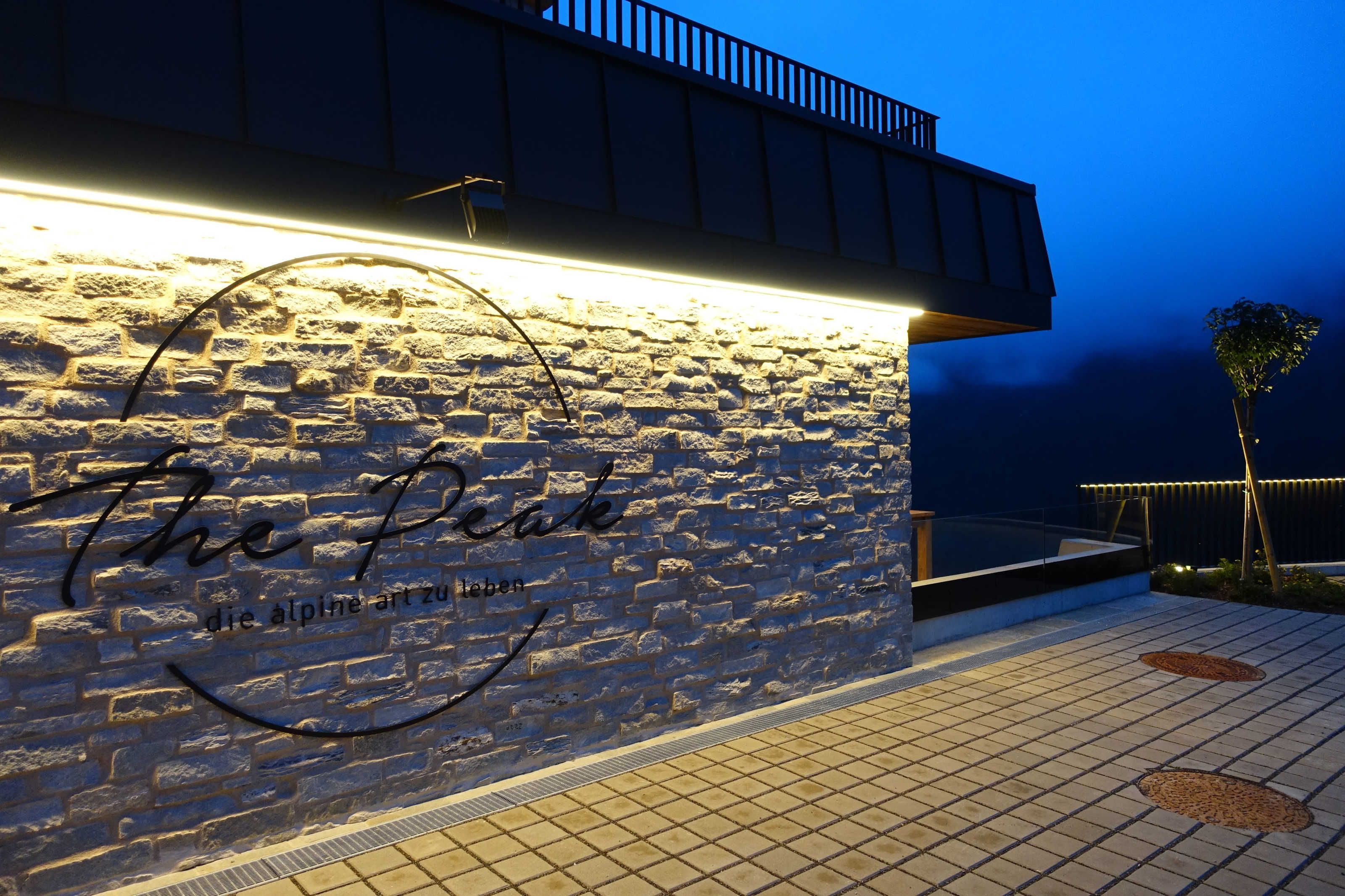 A stone wall with a sign that reads 'The Peak' and 'die alpine art zu leben'.