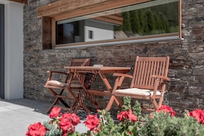 A patio with a table and chairs, a stone wall, and a window overlooking greenery.