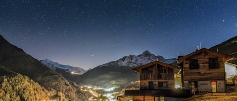 A mountain village at night with illuminated buildings and a starry sky.