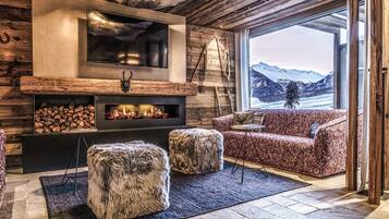 A cozy living room with a fireplace, a TV mounted on the wall, and a view of snow-capped mountains.
