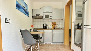 Cozinha compacta com área de refeições, micro-ondas, máquina de café e pequena geladeira.