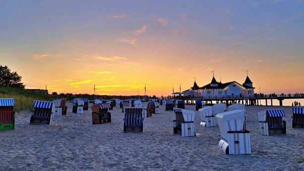 Uma praia com fileiras de cadeiras de praia e um píer com um edifício ao fundo.