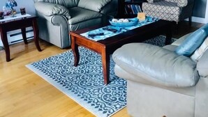 A living room with a grey leather sofa, a patterned armchair, a wooden coffee table, and a patterned rug.