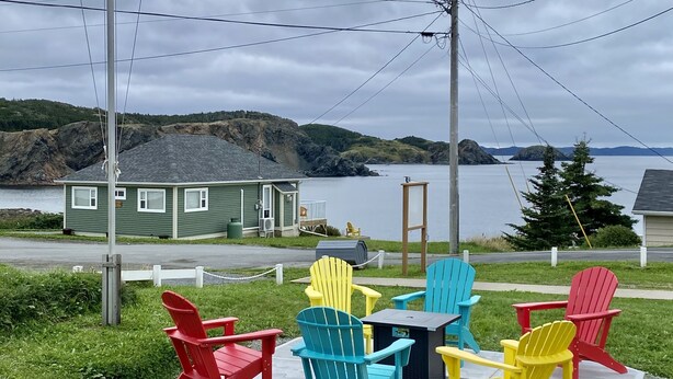 A waterfront property with a flagpole displaying the Canadian and UK flags, a green building, and colorful Adirondack chairs on a deck.