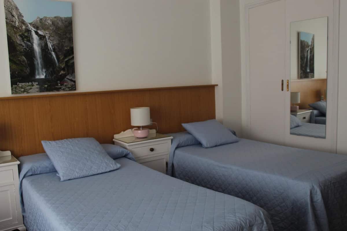 A hotel room with two beds, a wooden headboard, a nightstand with a lamp, and a painting of a waterfall.